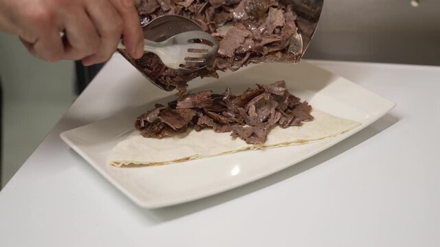 Professional chef arranging sliced doner meat over pide bread for an Iskender Kebab on a white plate, fa01