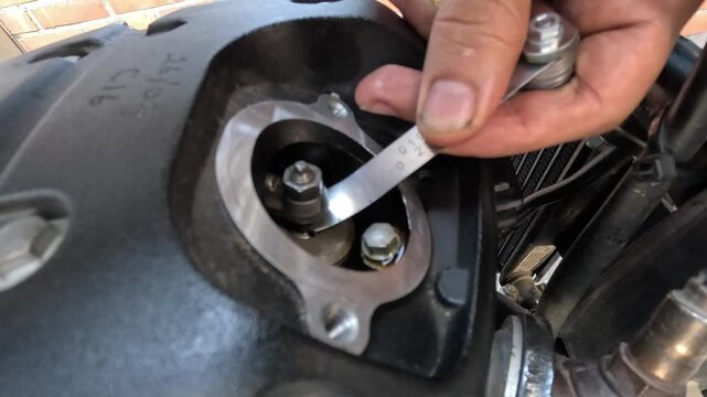 Close-up of a mechanic adjusting motorcycle engine valves using a feeler gauge.