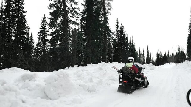 Two people riding snowmobile through snowy forest road with snowboards, winter travel adventure and outdoor lifestyle in mountains.
