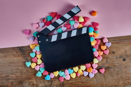 Clapper Board Surrounded by Colorful Heart-Shaped Candies on a Wooden Table
