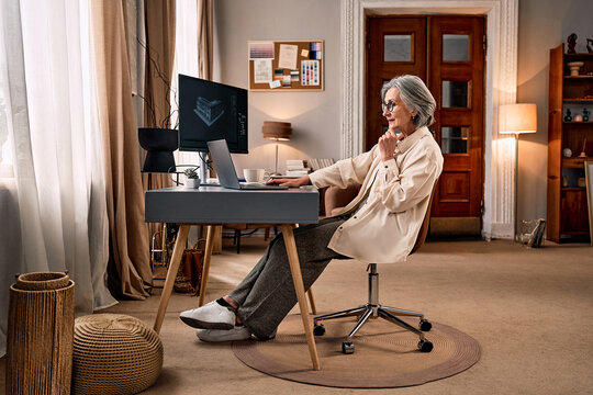 Creative work in a cozy home setting. An older woman sits at a desk in her home office, working on an architectural project.