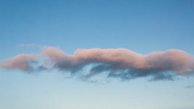 A single soft pink cloud floating in a clear blue sky during a peaceful golden hour sunset