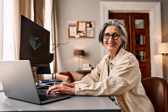 A beautiful mature woman working on a computer in a cozy modern office. Creative online work as a 3D artist and designer.