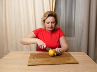 Fototapeta premium Woman sitting at kitchen table holding a cut apple on a wooden board near a knife, simple domestic food preparation.