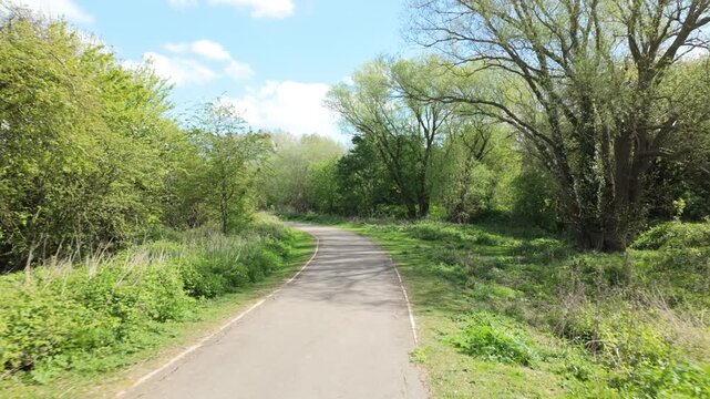 The Hamptons, Peterborough, England, UK - A PoV gimbal sequence walking on a spring day along a footpath with trees framing, and stunning bright blue sky and clouds overhead.