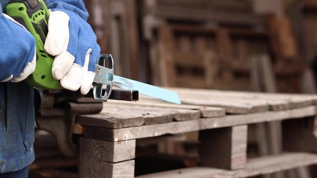 Cordless reciprocating saw cuts metal pipe. A craftsman in protective gloves uses a cordless reciprocating saw (electric knife) to saw a thin pipe. Working with a power tool. Close-up of work