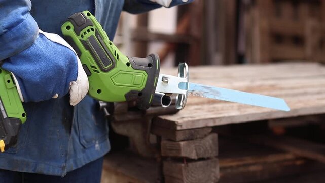 Cordless reciprocating saw cuts metal pipe. A craftsman in protective gloves uses a cordless reciprocating saw (electric knife) to saw a thin pipe. Working with a power tool. Close-up of work