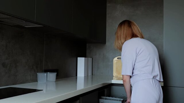 Woman in pajamas rearranges a toaster in a sleek, modern kitchen. The organized space showcases a stylish design, ideal for a refreshing morning routine