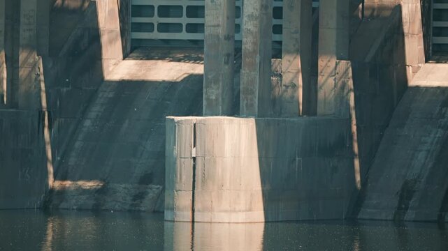 Massive hydroelectric dam. Strong geometric lines harsh shadows on brutalist concrete architecture. Muted colors imposing scale create powerful, stark industrial background
