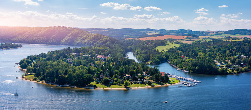 View of Slapy in Czechia showcasing the peaceful lake and surrounding lush greenery on a sunny day. Slapy reveals a tranquil lake surrounded by hills, dotted with boats and greenery. Slapy, Czechia.
