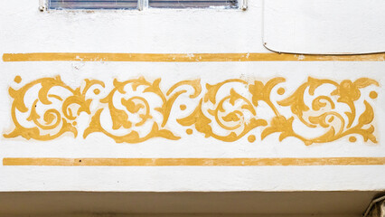 Ornamental Golden Floral Mural on White Stucco Wall With Decorative Scroll Border © Noel