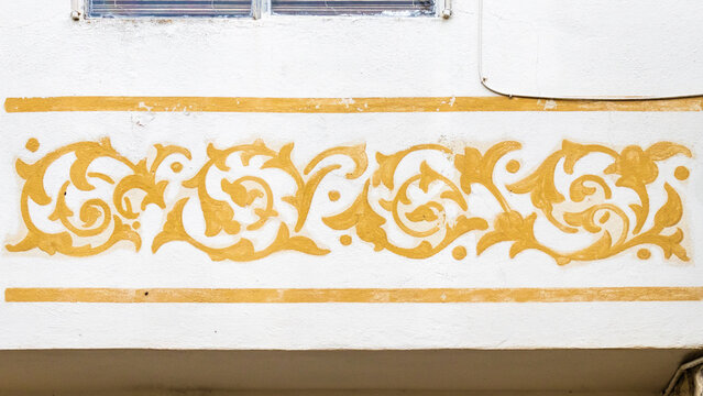 Ornamental Golden Floral Mural on White Stucco Wall With Decorative Scroll Border