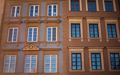 Fototapeta premium Classic Facades of Restored Townhouses in Warsaw Old Town: Decorative Window Frames with Golden Ornaments, Polish Architectural Heritage and Urban Travel Concept in Market Square