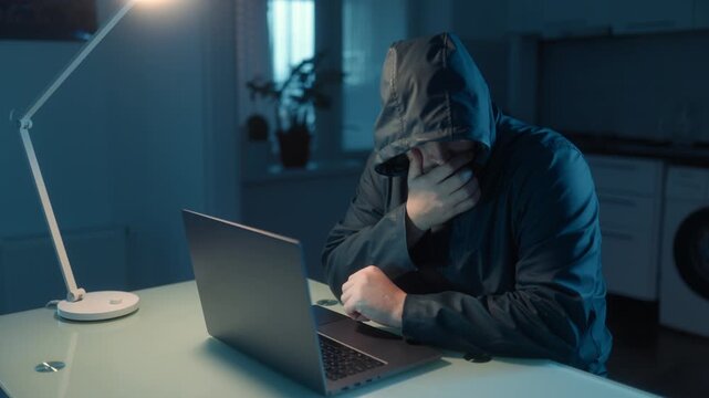 Medium Shot One Stressed Hacker In Hoodie Covering Face Near Laptop