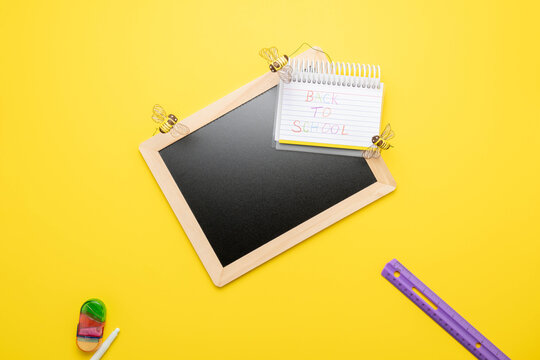 Blank chalkboard blackboard with a Back-to-school message on a spiral notebook with lined paper, yellow background with honey bee accents.