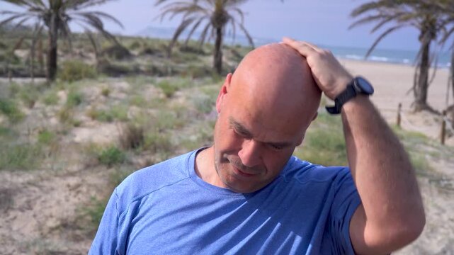 Man applies sunscreen on his shaved head on the beach