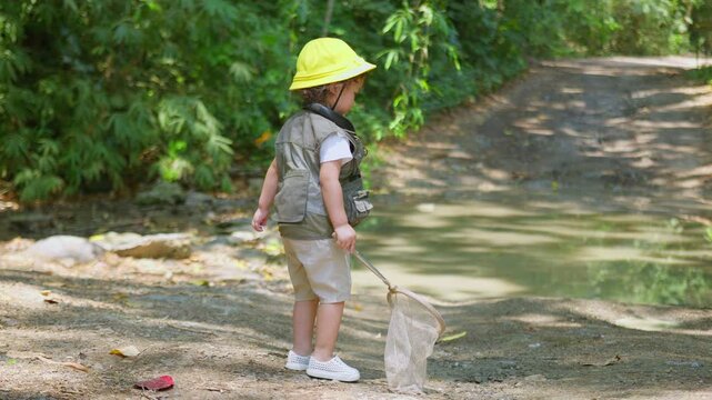 A curious toddler explorer with a butterfly net walks along a forest trail, engaging in nature discovery and experiential learning for childhood development.
