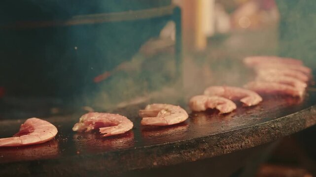 Grilled shrimp cooking on a round metal outdoor barbecue grill. Seafood preparing on hot surface. Culinary process of roasting crustacean for delicious meal.