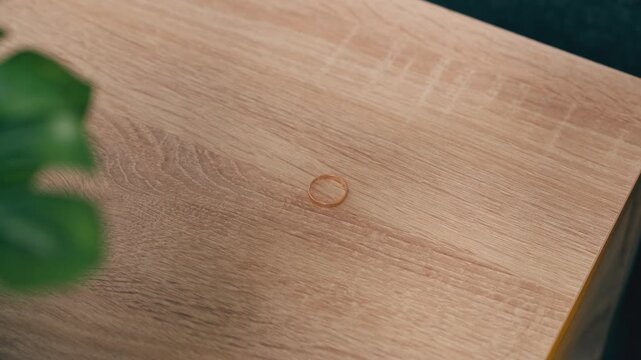 Woman's hand leaving gold wedding ring on wooden table representing divorce, separation, cheating, infidelity, heartbreak, and relationship problems