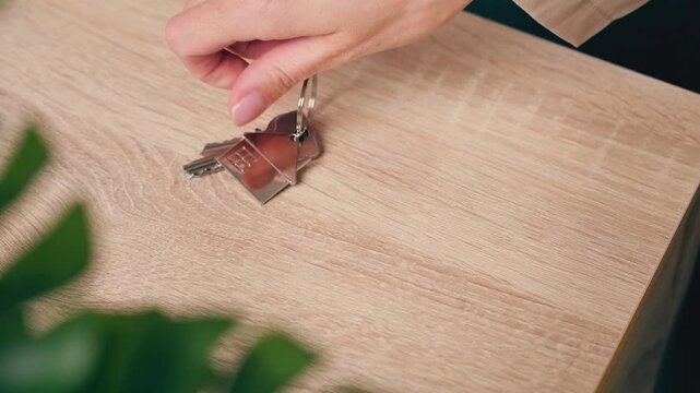Dramatic close-up of woman hand placing house keys and wedding ring on wooden table.Concept of emotional separation, relationship ending, significant life transition after difficult decision