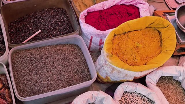 Indian spice bazaar featuring a vendor weighing dry coconut on a digital scale, surrounded by vibrant sacks of turmeric, chili powder, and assorted pulses. Traditional market scene with rich textures.