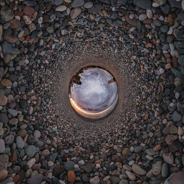 creative tiny planet photo of a rural landscape with dirt road, green fields, and cloudy sky forming a circular world.