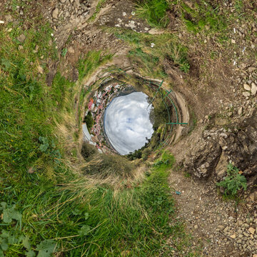 creative tiny planet photo of a rural landscape with dirt road, green fields, and cloudy sky forming a circular world.