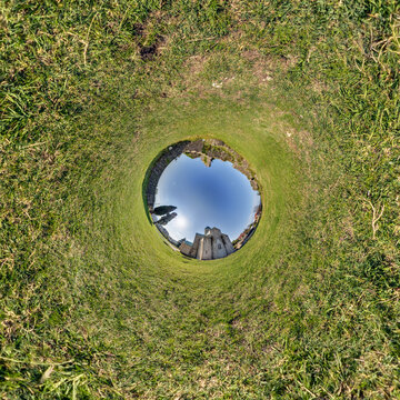 creative tiny planet photo of a rural landscape with dirt road, green fields, and cloudy sky forming a circular world.