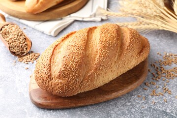 Naklejka premium Loaf of bread with sesame seeds, grain and spikes on grey table, closeup