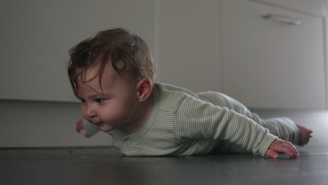 Baby lying flat on kitchen floor lifting head with expressive face showing curiosity and effort in soft domestic light