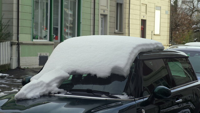 Car parked on snowy street covered with thick snow layer on roof and windshield, symbol of cold winter day and frozen urban environment