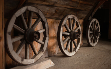 Obraz premium Close-up of Three Vintage Wooden Wagon Wheels. Detailed Architectural Shot of Antique Transportation Components Leaning Against a Timber Wall with Selective Focus and Natural Light.