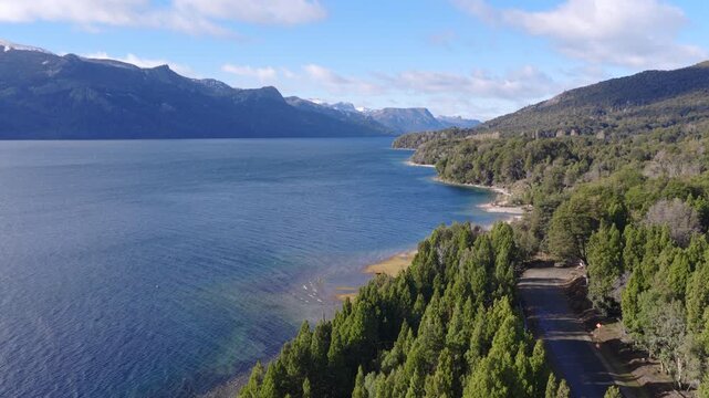 Aerial view of pickup truck driving along scenic road toward Villa Traful by lake in Patagonia, Argentina.