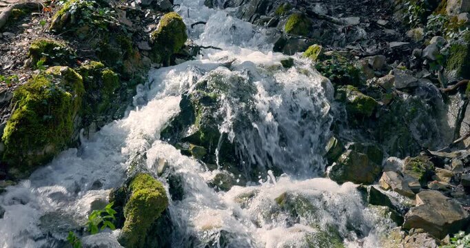 Cascade waterfall falling on rocks in spring sunny forest, slow motion