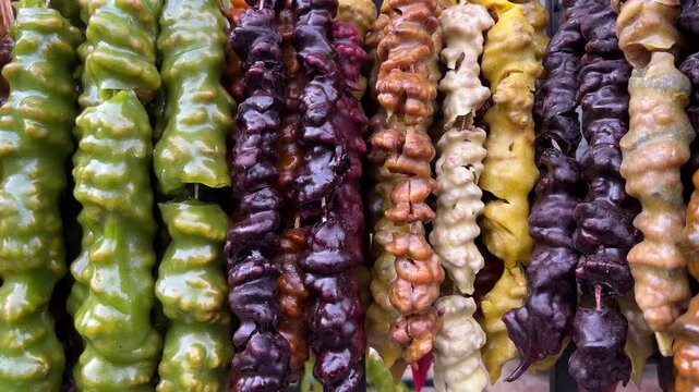 Horizontal 4K video. Georgian dish green, red, yellow, brown churchkhela hanging on rope on harvest fair, city holiday Tbilisoba, Christmas festival, New Year market, pastry shop. Sweet sugar food
