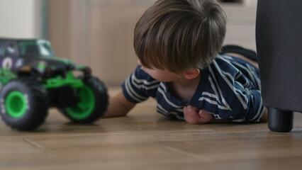 Little boy lying on wooden floor playing quietly with toy monster truck in soft daylight childhood innocence imagination and simple domestic moment of play © Marco