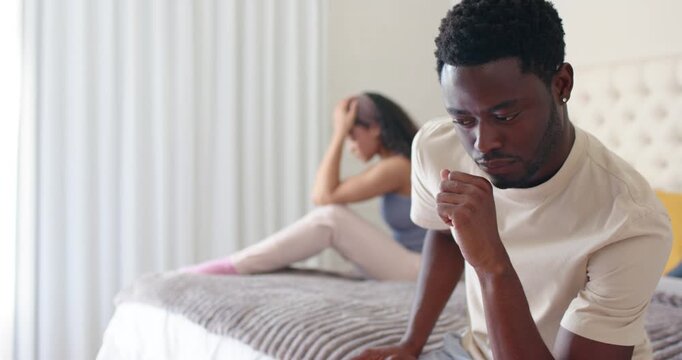 African American couple sitting on bed after fight man holding mouth woman rubbing head, copy space