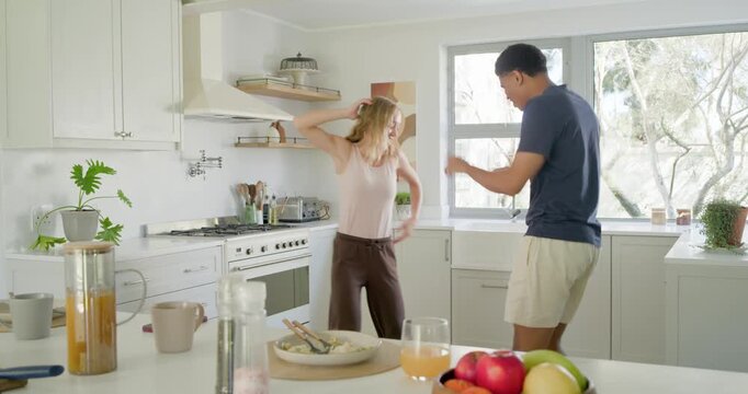 Diverse couple dancing, catching each other's eye, mirroring steps at kitchen island with fruit
