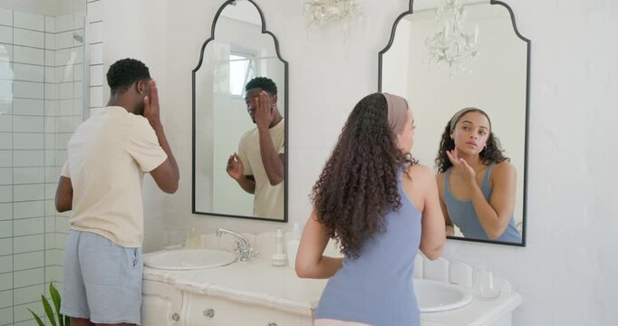 African American couple preparing at marble double vanity, male rubbing jaw as female dabbing eyes
