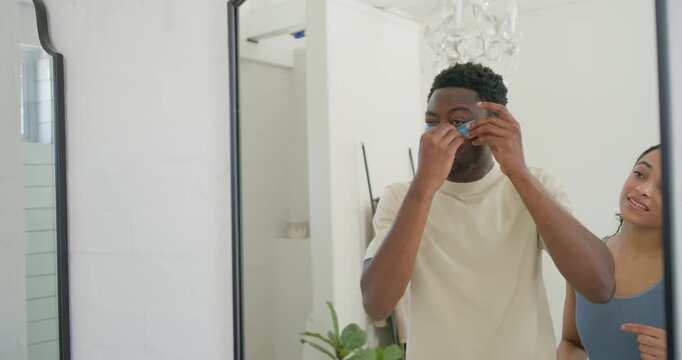 African American couple at mirror man opening jar placing blue patches woman tweaking for skincare