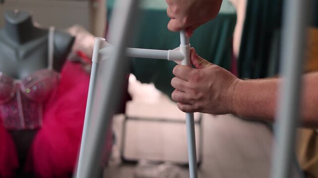 Defocused 4K video. 60 fps. Male hand inserting metal pipe into white plastic rail. Process of assembling inexpensive new cheap rack with fabric shelf. DIY, easy construction, decorating flat, room