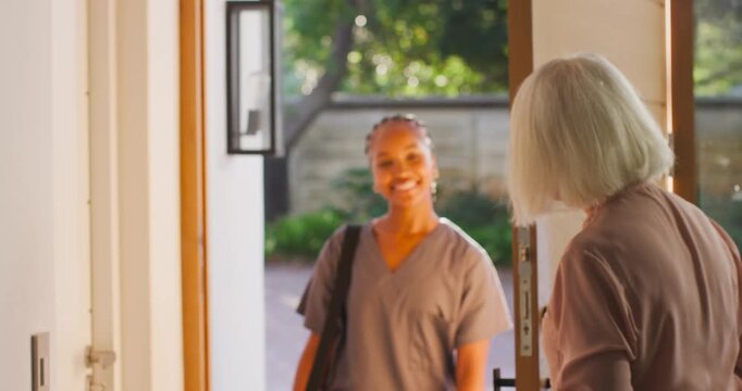 Caregiver carrying bag in scrubs reaching handle opening door hugging senior woman at home visit