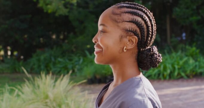 African adult woman walking garden path to wooden door, reaching and knocking, wearing gray scrubs