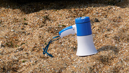 A hand-held megaphone lies in the sand on the sea beach. © ROMAN DZIUBALO