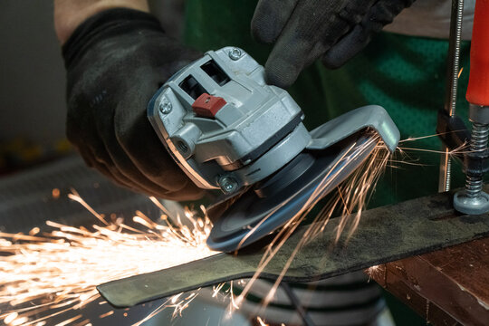 mechanik ścierający metal szlifierką elektryczną trzymaną w dłoniach chronionych rękawiczkami, snop iskier  lecący spod szlifierki