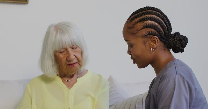 African American caregiver checking in speaking on sofa as Senior woman listening touching necklace