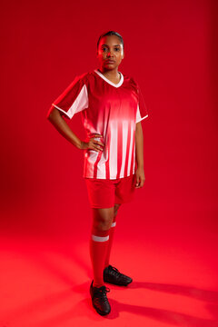 African American woman posing in red studio wearing soccer jersey, red shorts, red socks and cleats