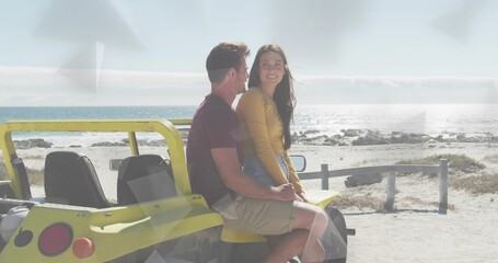 Naklejka premium Sitting couple smiling, holding on yellow dune buggy at beach, wearing mustard top and maroon tee