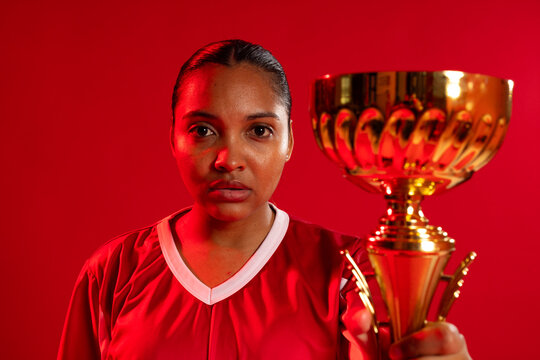 African American woman standing against red backdrop in red jersey white V-neck holding gold trophy