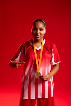 Adult African woman standing in studio against red backdrop, wearing striped jersey and gold medal